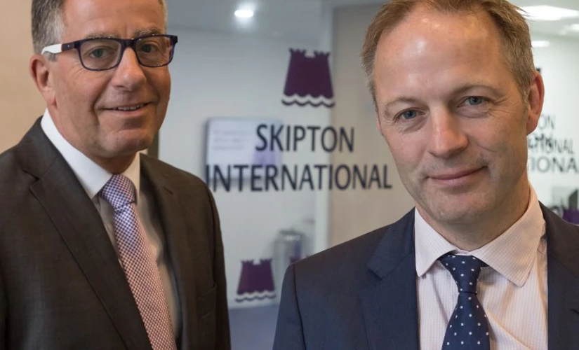 Two men smiling Infront of Skipton logo