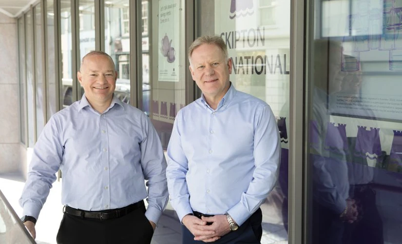 Two men smiling Infront of Skipton logo