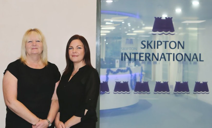 two women smiling Infront of Skipton International logo