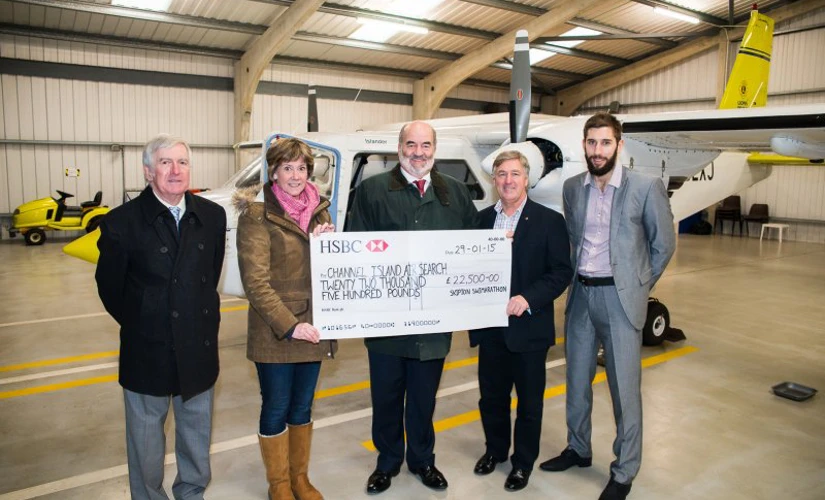 Group of people smiling in front of plane with cheque